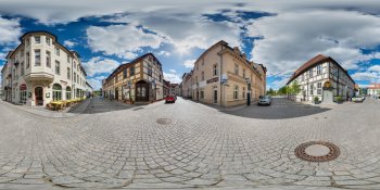 Panoramic view of a European town square with cobblestone pavement, historic buildings, and a bright blue sky.